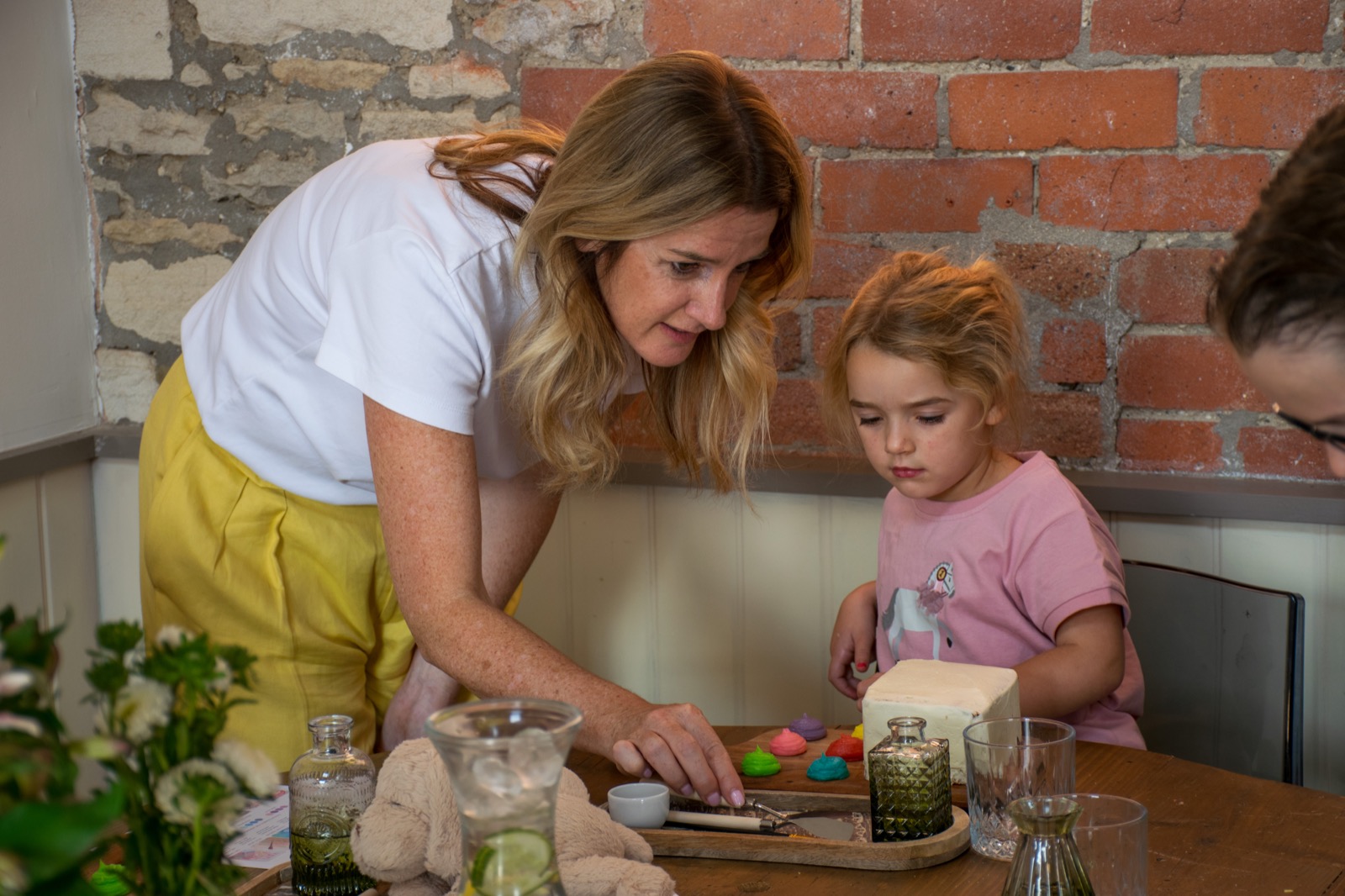 An adult helping a young guest with icing at the table
