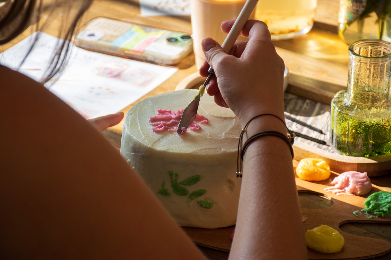 Hands working together to decorate a cake with colourful icing