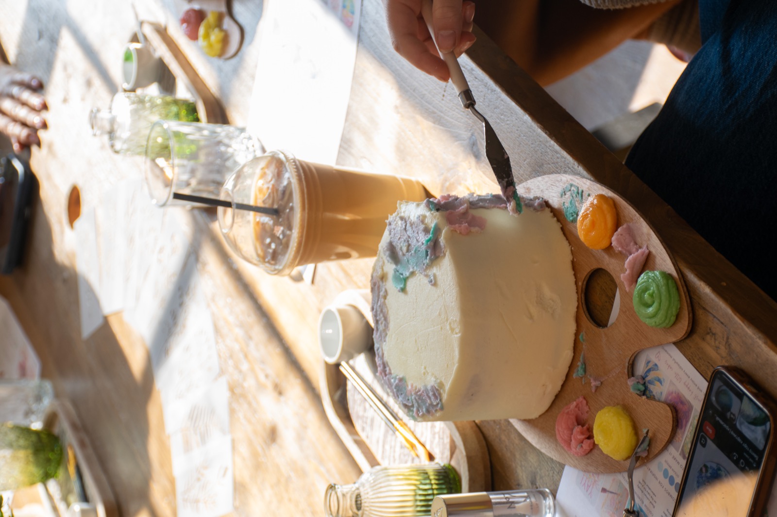A guest decorating a cake beside a drink at the workshop table