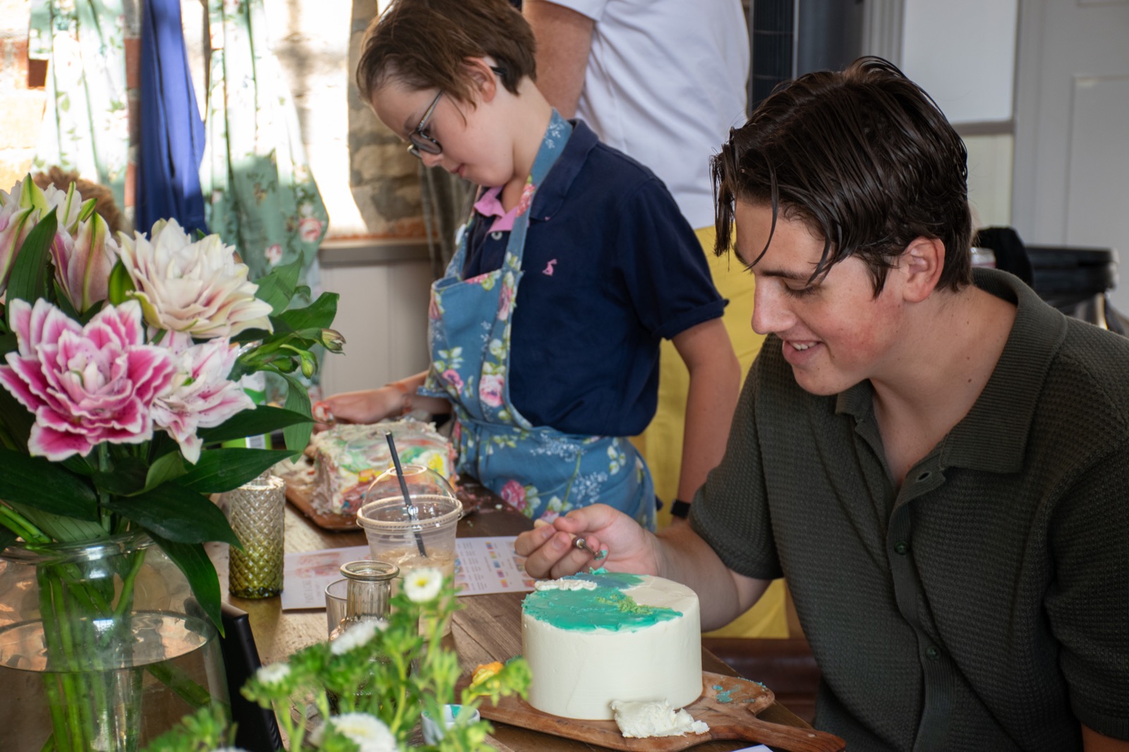An adult and child painting cakes together at the workshop table