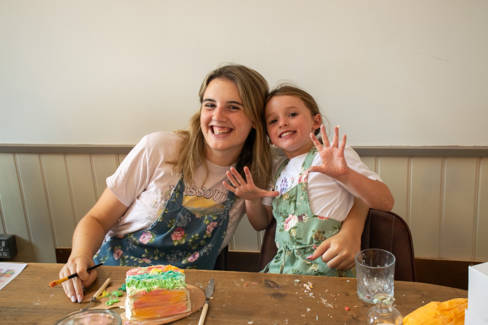Two guests smiling and showing their icing-covered hands beside a colourful cake